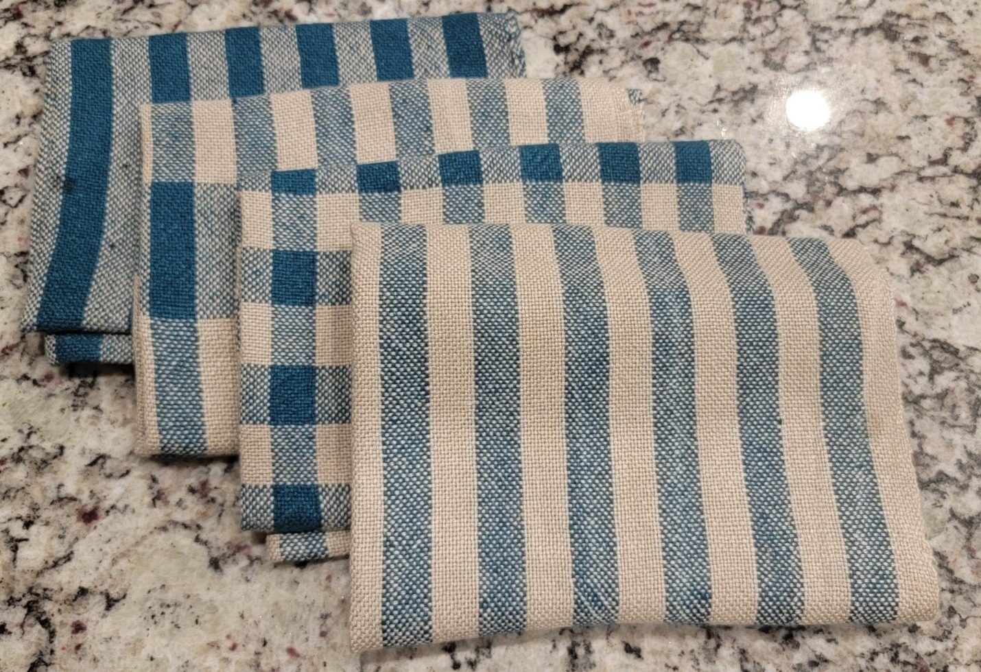 Stack of folded handwoven towels in blue stripe and check patterns on a granite counter
